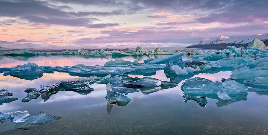 Dramatic scene of blue ice flows with purple and peach colors in a cloudy sky.